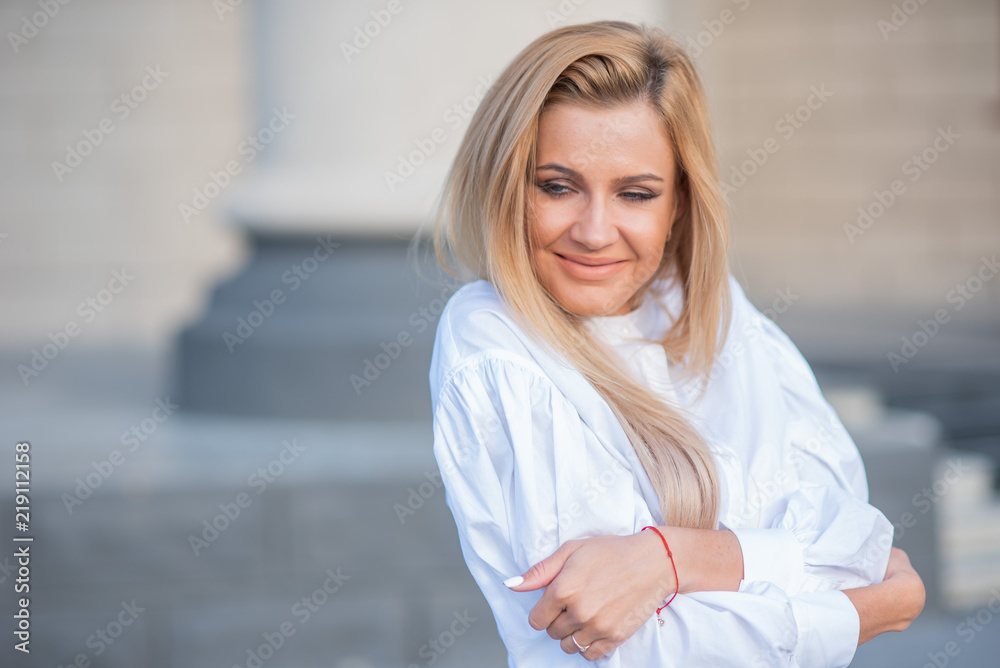 portrait of a blonde on a building background with columns. beautiful blonde in a white blouse smiling portrait of a blonde on a building background with columns. beautiful blonde in a white blouse smiling