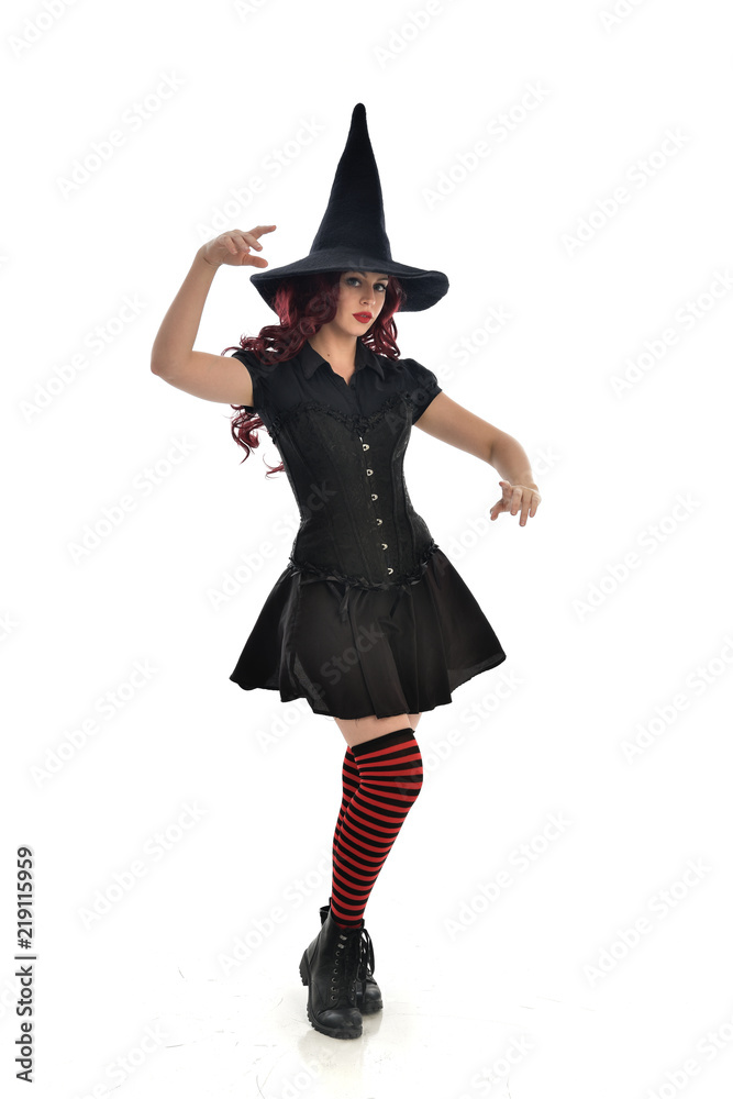 full length portrait of red haired girl wearing black witch costume and pointy hat. standing pose, isolated on white studio background. full length portrait of red haired girl wearing black witch costume and pointy hat. standing pose, isolated on white studio background.