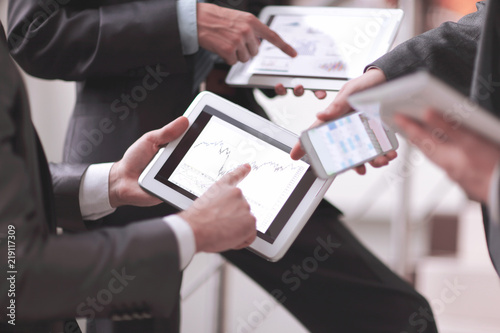 Businessmen at meeting presenting charts on smartphone, tablet