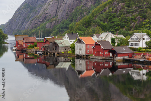 Bright old wooden houses of small domestic Norwegian village reflect in the fjord under the cloudy sky in Rogaland country, Norway