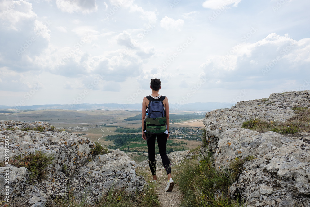 Obraz premium young woman standing on top of a hill and looking forward to the plain. Female hiker on top of mountain enjoying view. Travel, freedom, vacation, trekking, hiking concept