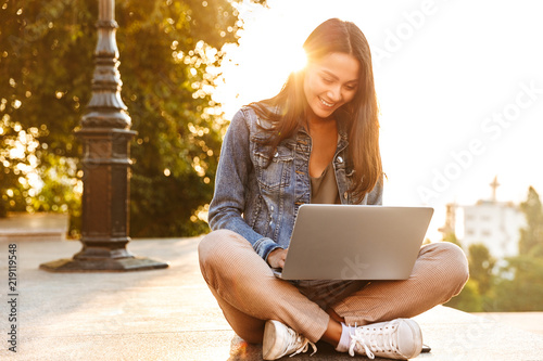 Smiling young asian girl using laptop while sitting photo