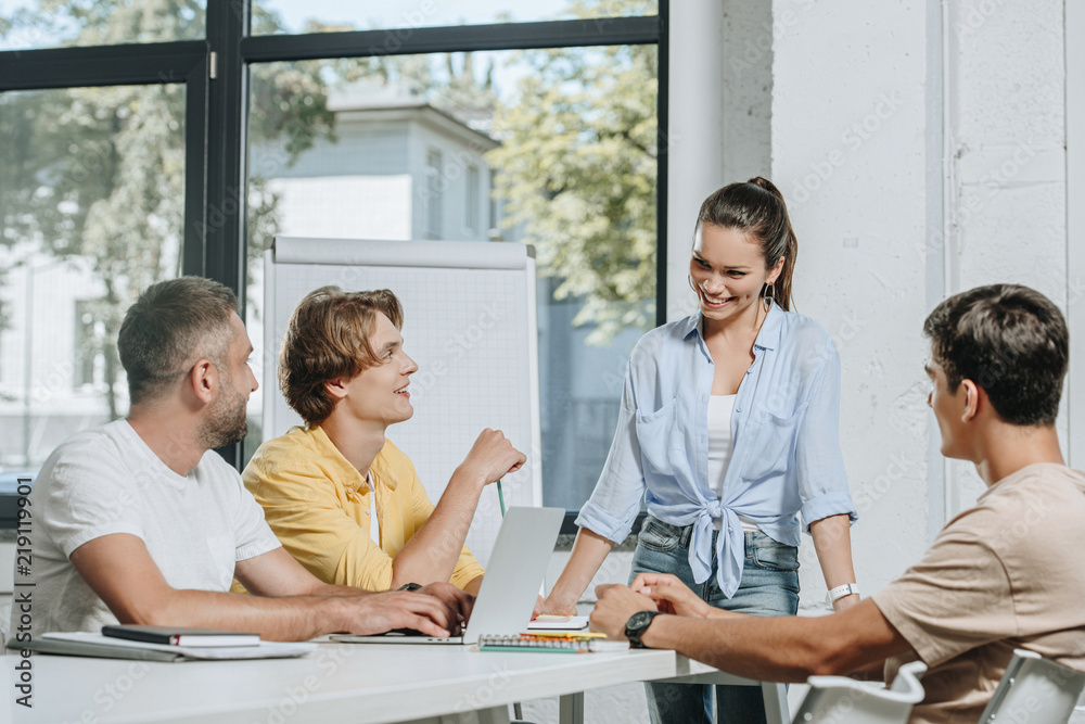 businessmen sitting at table during meeting and looking at businesswoman in office businessmen sitting at table during meeting and looking at businesswoman in office