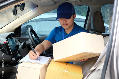 Portrait of a delivery Asian man courier writing on a clipboard while sitting in a delivery van