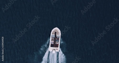 Direct overhead shot of young man driving outboard motor boat across glassy lake photo