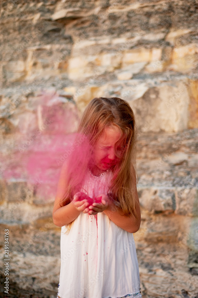 A little girl with palms blowing on the paint Holi pink. Great moment. A little girl with palms blowing on the paint Holi pink. Great moment.