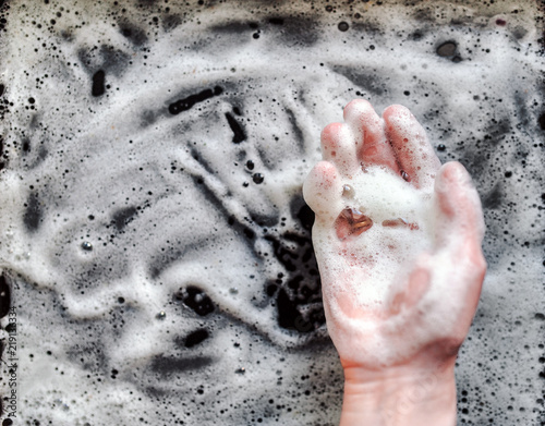 The housewife uses washing-up liquids. The hand washes the dirty surface with a soap solution. photo