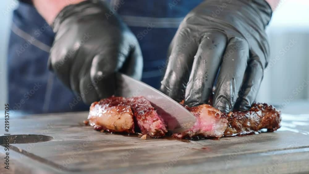 Chef cuts juicy meat stake on the wood board with the knife, close-up