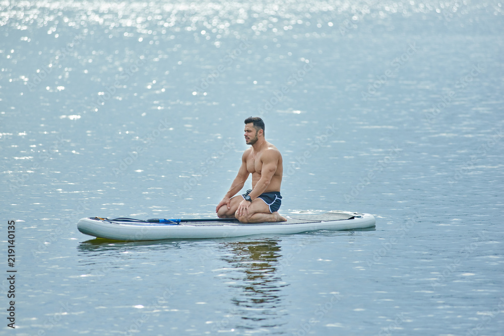 Sporty man sitting on sup board during trainining on lake, looking forward. Sporty man sitting on sup board during trainining on lake, looking forward.
