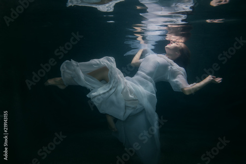 Beautiful woman in a white dress swims under the water.