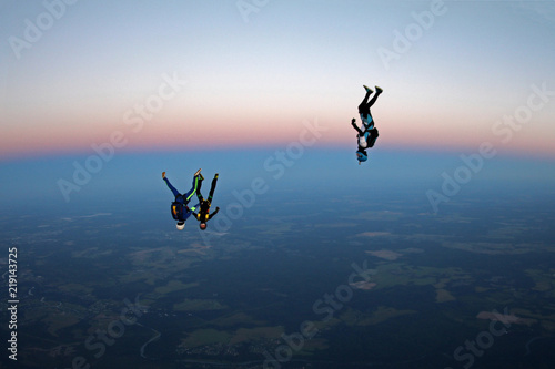 Three skydivers are falling in the evening sky.