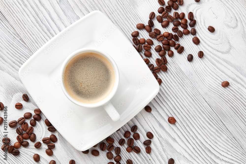 Obraz premium cup of coffee with coffee's beans over white wooden background, top view