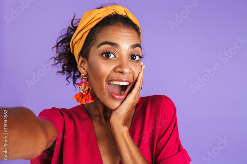 Cheerful african woman in dress having fun and making selfie