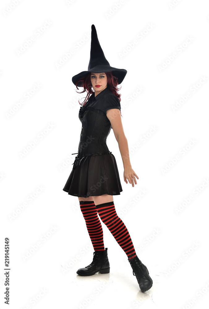 full length portrait of red haired girl wearing black witch costume and pointy hat. standing pose, isolated on white studio background. full length portrait of red haired girl wearing black witch costume and pointy hat. standing pose, isolated on white studio background.