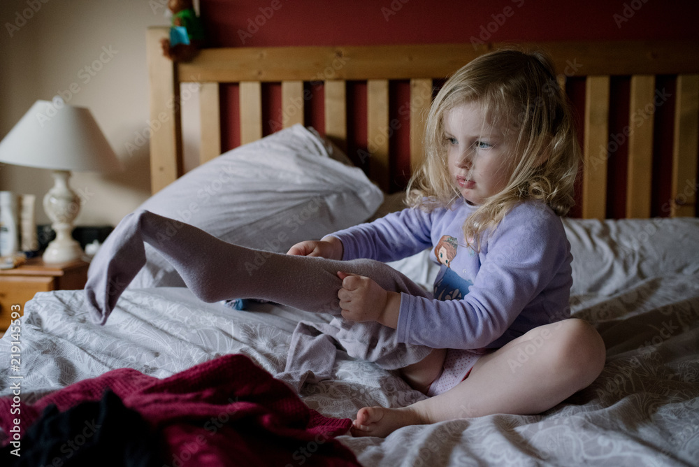 Little girl putting on her tights all by herself on her parents bed