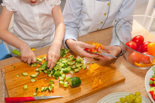Children cut cucumber, tomato and pepper on kitchen board