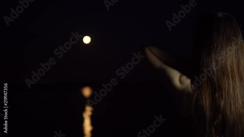 A young woman with dark hair admires the red new moon, a rare astronomical phenomenon. The girl stands with her back to the camera on the river bank. photo