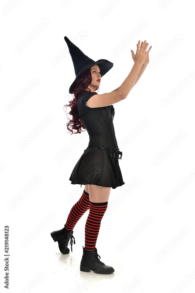 full length portrait of red haired girl wearing black witch costume and pointy hat. standing pose, isolated on white studio background. full length portrait of red haired girl wearing black witch costume and pointy hat. standing pose, isolated on white studio background.