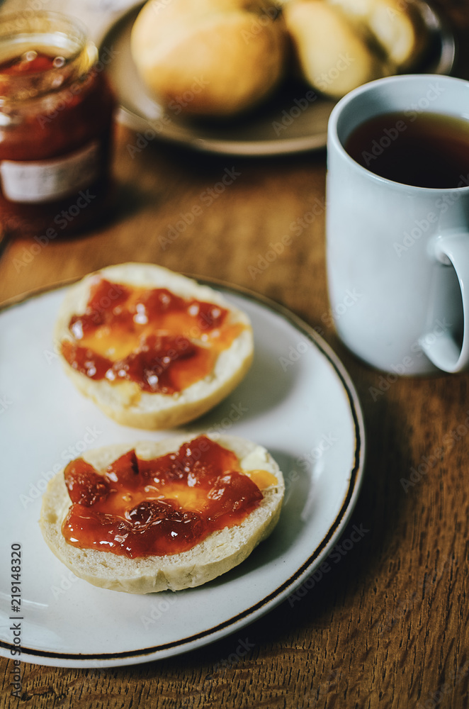 Cup of black tea with red jam on bread buns for tasty breakfast. Simple and delicious breakfast idea. Wooden table background.