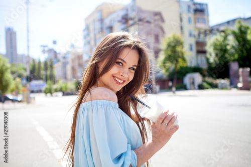young beautiful brunette drinking coffee walking around the city.wearing blue blouse portrait of smiling girl with well-groomed long dark hair