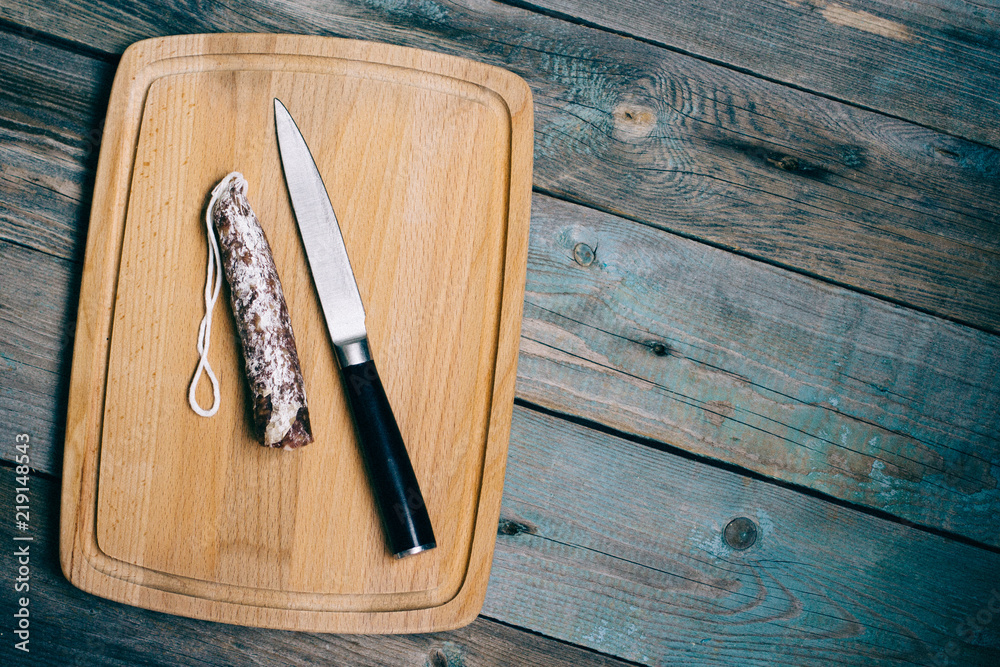 top view smoked sausage, salami, knife on cutting Board, wooden background