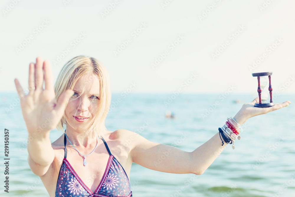 Woman with an hourglass against the sea, ocean. The concept of leisure, free time.