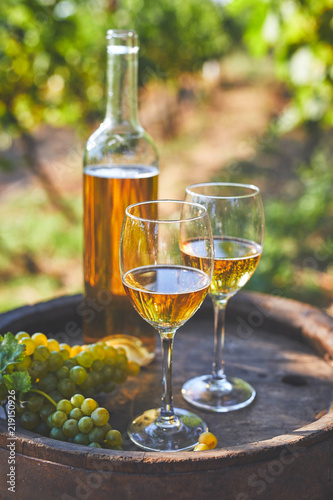 Two glasses of white wine with a bottle on a wooden barrel