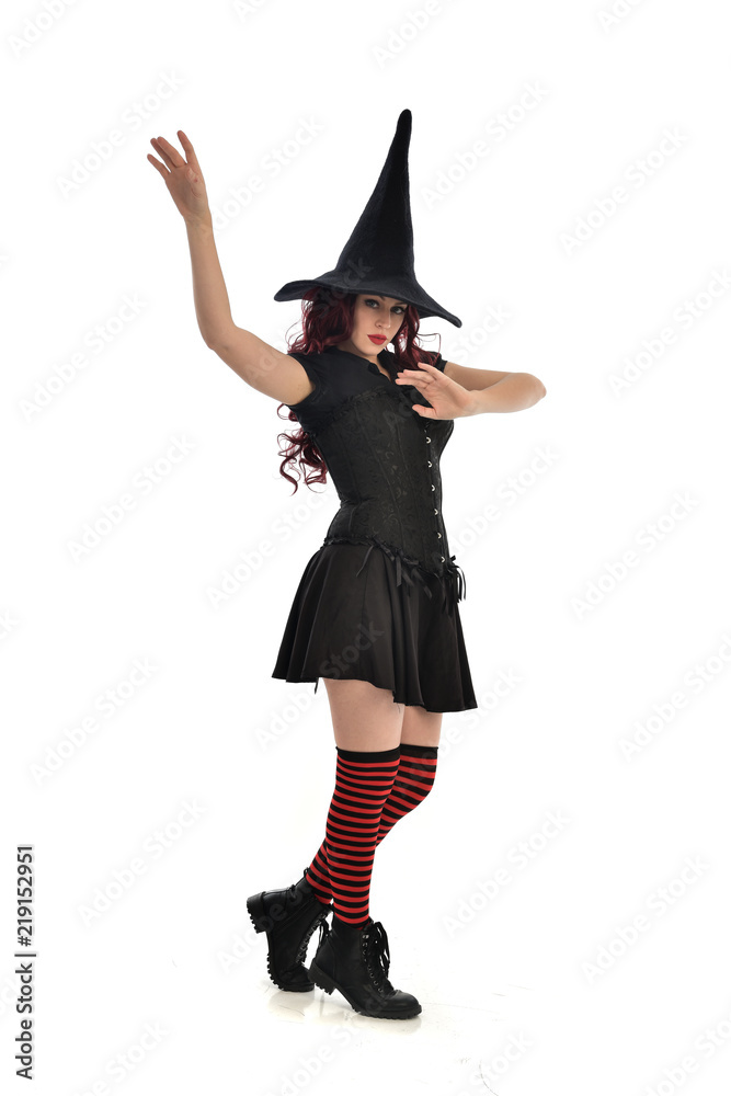 full length portrait of red haired girl wearing black witch costume and pointy hat. standing pose, isolated on white studio background. full length portrait of red haired girl wearing black witch costume and pointy hat. standing pose, isolated on white studio background.