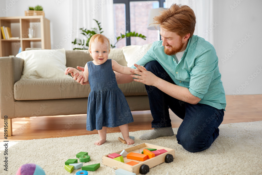 family, fatherhood and people concept - red haired little baby girl standing with father help at home family, fatherhood and people concept - red haired little baby girl standing with father help at home