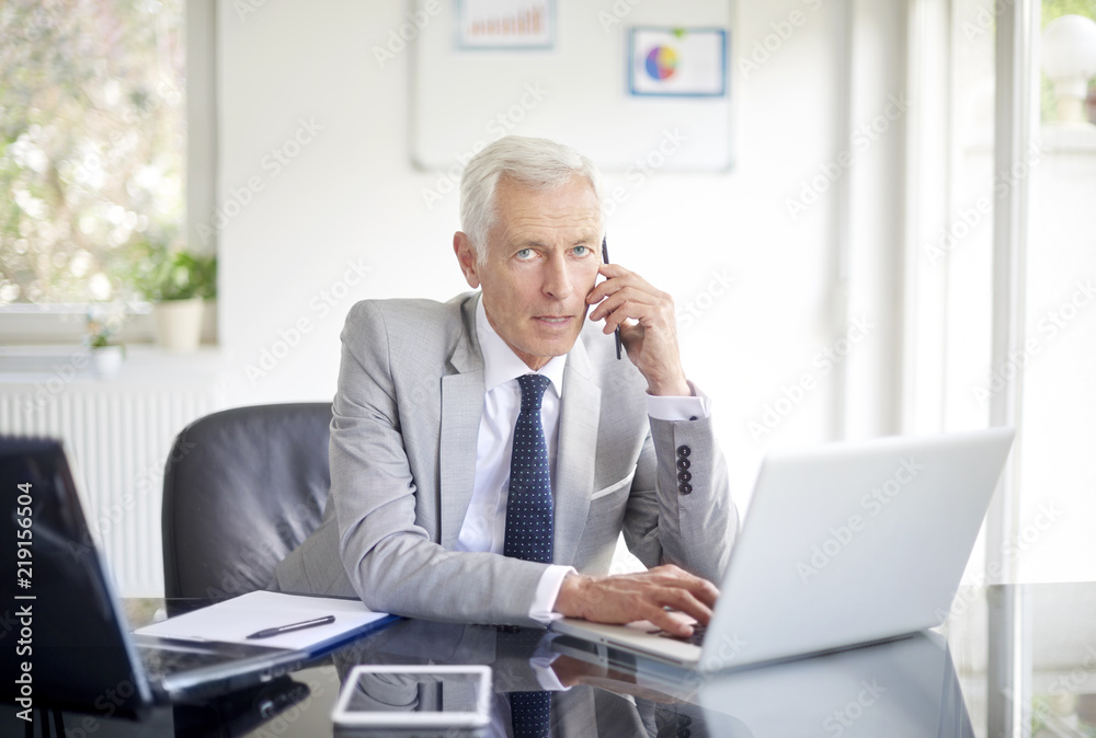 Thinking businessman making call and using laptop in the office Thinking businessman making call and using laptop in the office