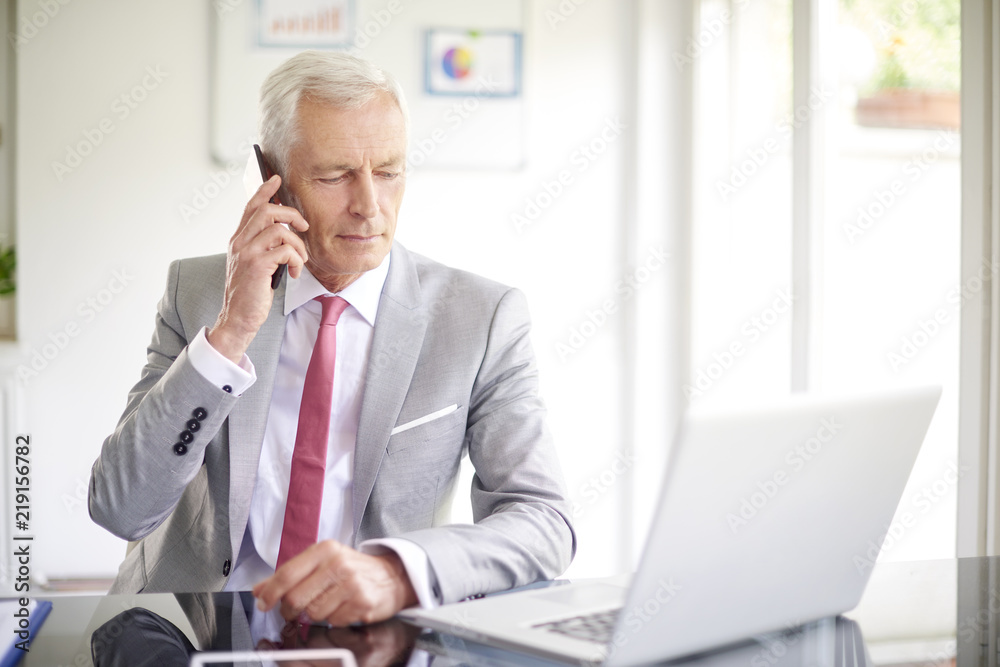 Thinking businessman making call and using laptop in the office Thinking businessman making call and using laptop in the office