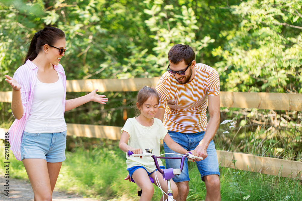 Fototapeta premium koncepcja rodziny, rodzicielstwa, wypoczynku i ludzi - szczęśliwa matka, ojciec i córeczka uczą się jeździć na rowerze w letnim parku