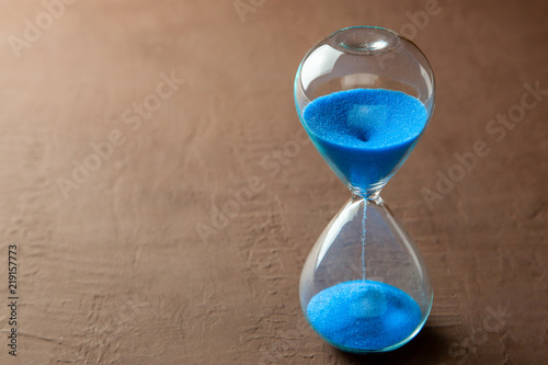 Hourglass with blue sand on brown background