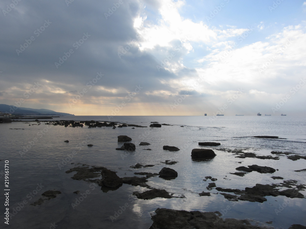 Rocks landscape sea with giants cumulonimbus clouds in the sky and cargo ships at the horizon . Livorno, Tuscany, Italy