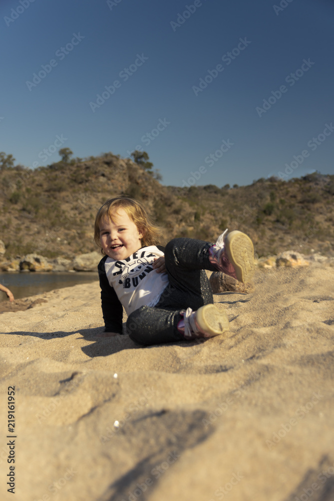 Beautiful little girl playing with sand on the beach in Cordoba, Argentina, during a sunny winter afternoon