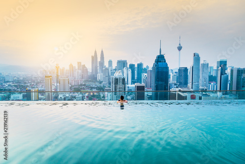 Canvas Print Asian businessman relax in swimming pool on roof top behind beautiful city view