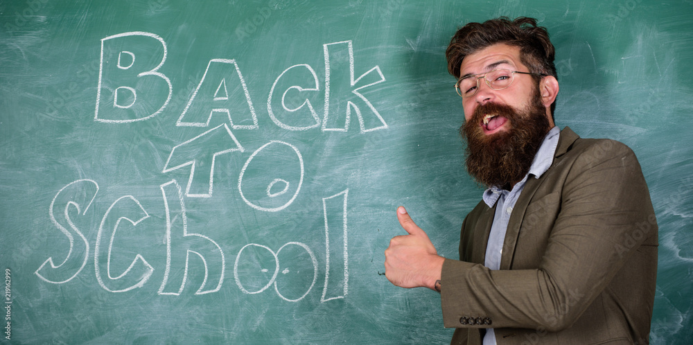Teacher or educator welcomes students while stands near chalkboard with inscription back to school. Ready to teach you. Teacher begin first lesson after holidays. School and studying concept
