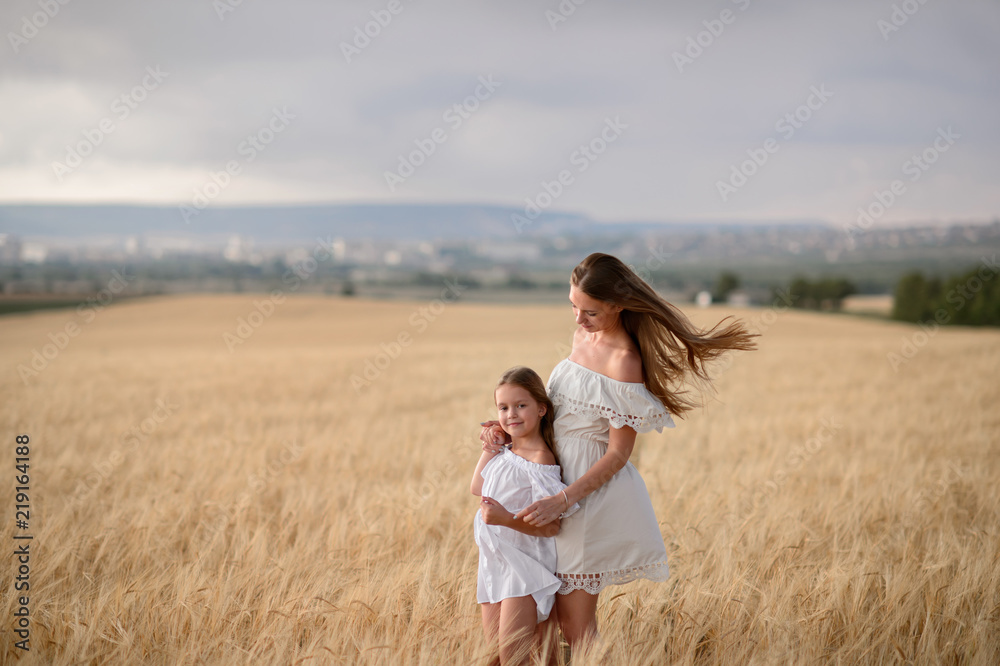 Beautiful family in a field of rye at sunset. A woman and child in amazing clothes walking through the field of rye.