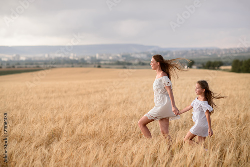 Beautiful family in a field of rye at sunset. A woman and child in amazing clothes walking through the field of rye.