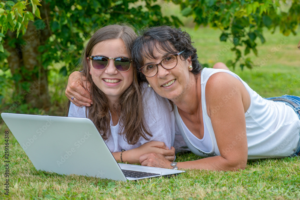 smiling mom and daughter using a laptop at garden smiling mom and daughter using a laptop at garden