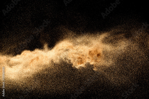 Dry river sand explosion. Golden colored sand splash agianst dark background.