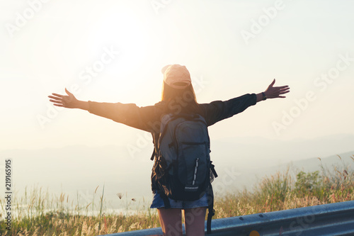Freedom traveler woman standing with raised arms and enjoying a beautiful nature and cheering young woman backpacker at sunrise seaside mountain peak