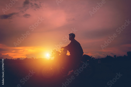 Silhouette of biker man  with his motorbike,he shoulder backpack. beside the natural lake and beautiful, enjoying freedom and active lifestyle, having fun on a bikers tour.sunset background and sky.