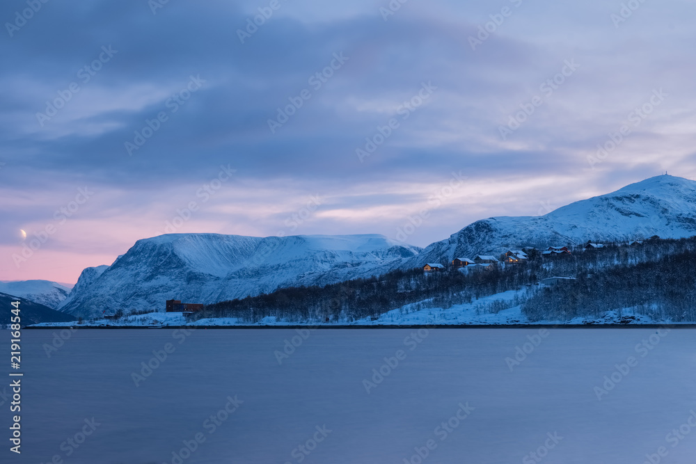 Landscape of a Norwegian fjord and town in winter at sunset.