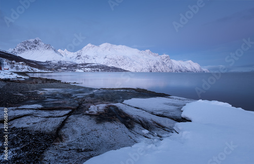 Landscape of Norway in winter at blue hour. Norwegian coastline in winter. Mountain covered with snow at the background.