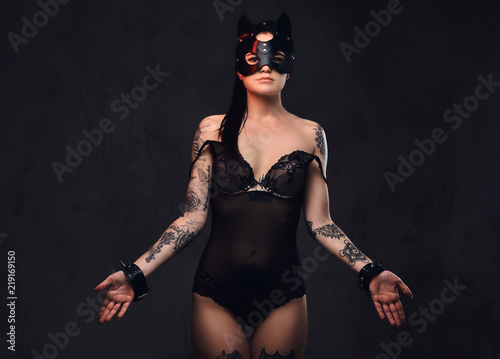 Sexy woman wearing black lingerie in BDSM cat leather mask and accessories posing on dark background. 