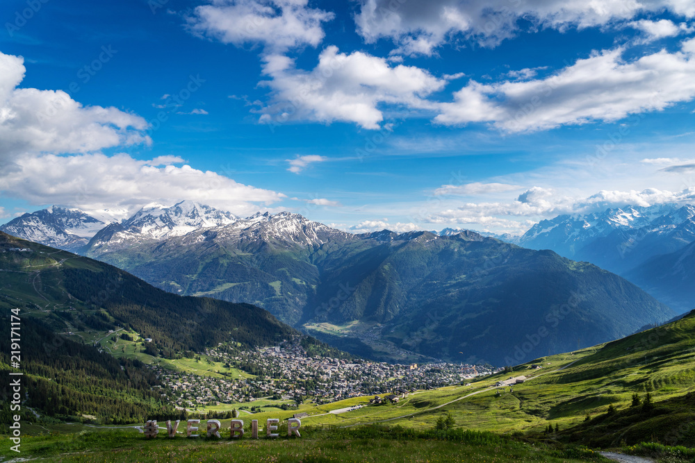 Scenery view of Verbier village surrounded with beautiful Swiss Alps mountains in sunny summer day with green meadows, forests, blue sky.