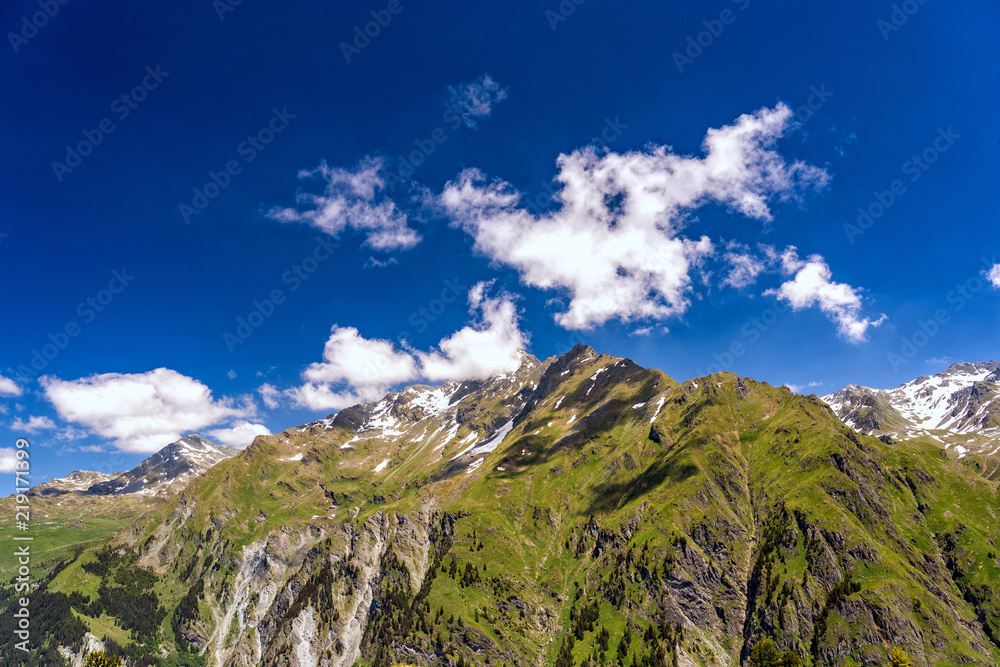 Obraz premium Scenic view of beautiful landscape in Swiss Alps. Fresh green meadows and snow-capped mountain tops in the background in springtime, Switzerland.