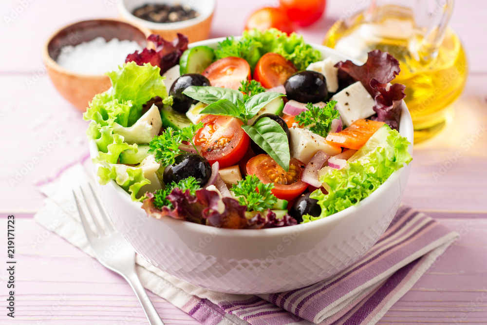 Fresh Greek salad with vegetables, feta cheese and black olives in white bowl on purple wooden background