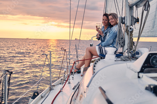 Female friends relaxing on the yacht with glasses of wine in the hands, during sunset on the high seas. © Fxquadro